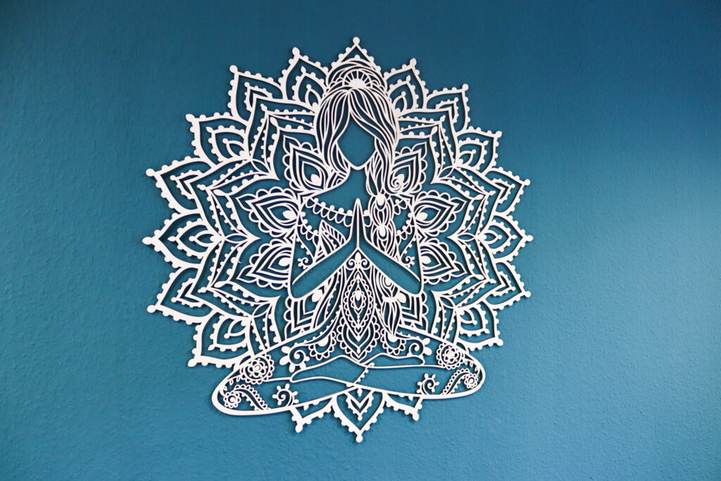 Ein Mandala mit einer Frau im Schneidersitz hängt an einer blauen Wand.