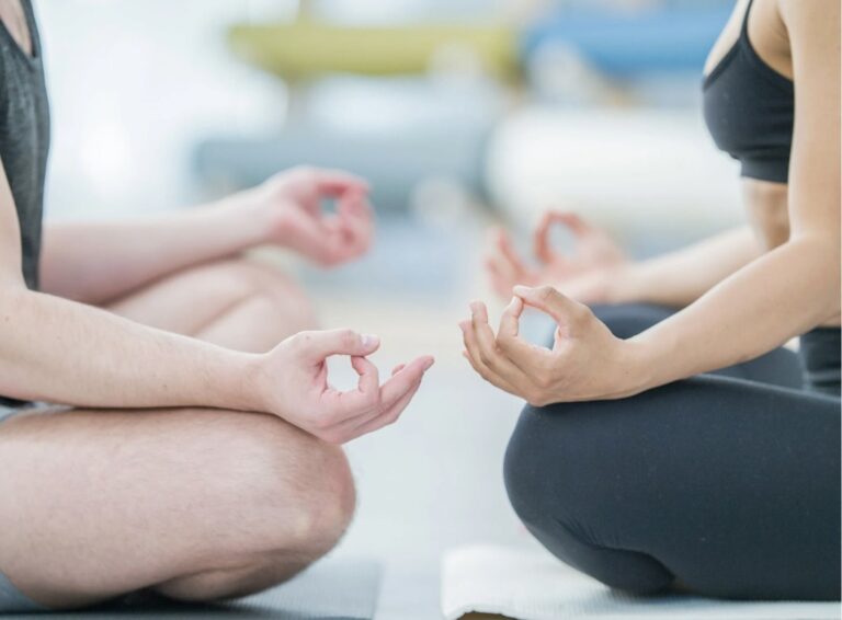 Zwei Personen sitzen sich im Schneidersitz gegenüber.