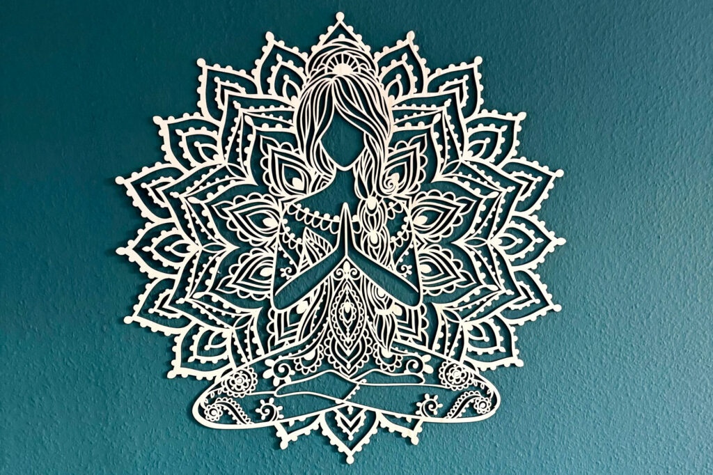 Ein Mandala mit einer Frau im Schneidersitz hängt an einer blauen Wand.
